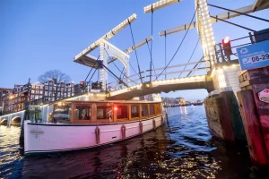 Abendaufnahme der Saloonsloep unter einer Brücke in Amsterdam