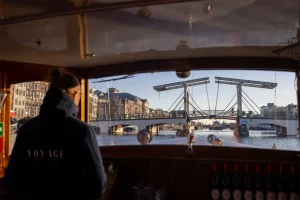 Kapitän auf der Saloonsloep mit Blick auf eine Amsterdamer Brücke