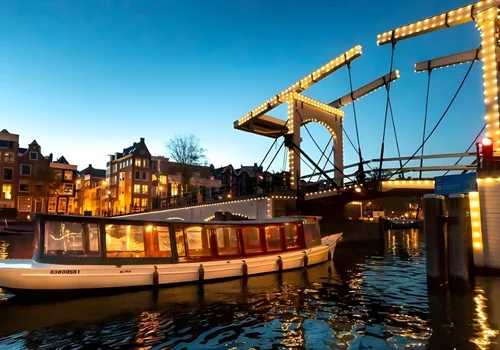 Salonboot das durch eine Brücke fährt am Abend in Amsterdam
