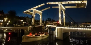 Ein Boot fährt abends unter einer Brücke in Amsterdam hindurch
