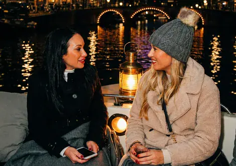 Twee vriendinnen met mutsen borrelen 's avonds op een boot tijdens het Light Festival